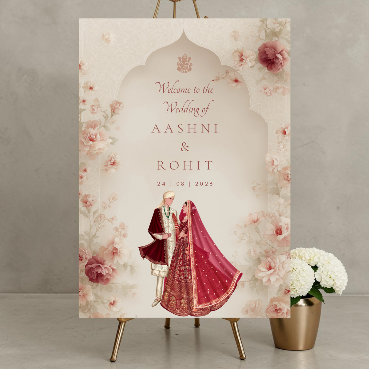 Personalised Hindu wedding welcome sign on 3mm foamex displayed on gold easel featuring Ganesh symbol, illustrated bride in crimson red lehenga and groom in red sherwani within soft cream Mughal arch surrounded by blush and mauve watercolour peonies