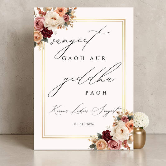 Personalised Ladies Sangeet welcome sign printed on 3mm Foamex, 
featuring burgundy blush and ivory floral arrangement, gold border 
frame and elegant calligraphy script reading Sangeet Gaoh Aur Giddha 
Paoh with custom name Kiran and date, A1 size, leaning against grey wall
