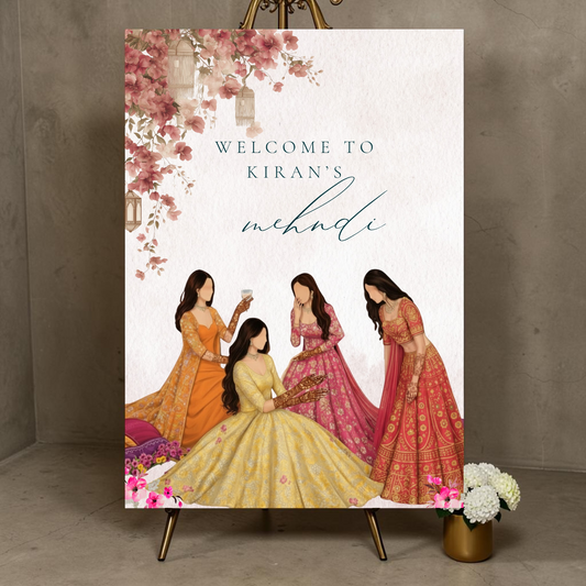 Personalised mehndi welcome sign on an easel showing a bride seated in a yellow lehenga surrounded by bridesmaids in orange and red, with pink floral garlands at the top