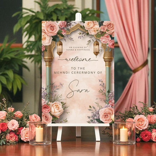 Close-up of Mehndi ceremony sign showing personalised bride name in flowing script font beneath gold Moroccan lanterns with henna and happiness tagline on blush watercolour background