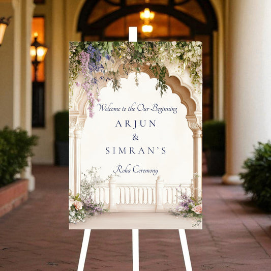 Close-up of Roka ceremony sign showing Welcome To Our Beginning tagline and personalised couple names in navy serif and script fonts beneath wisteria floral arch on cream background