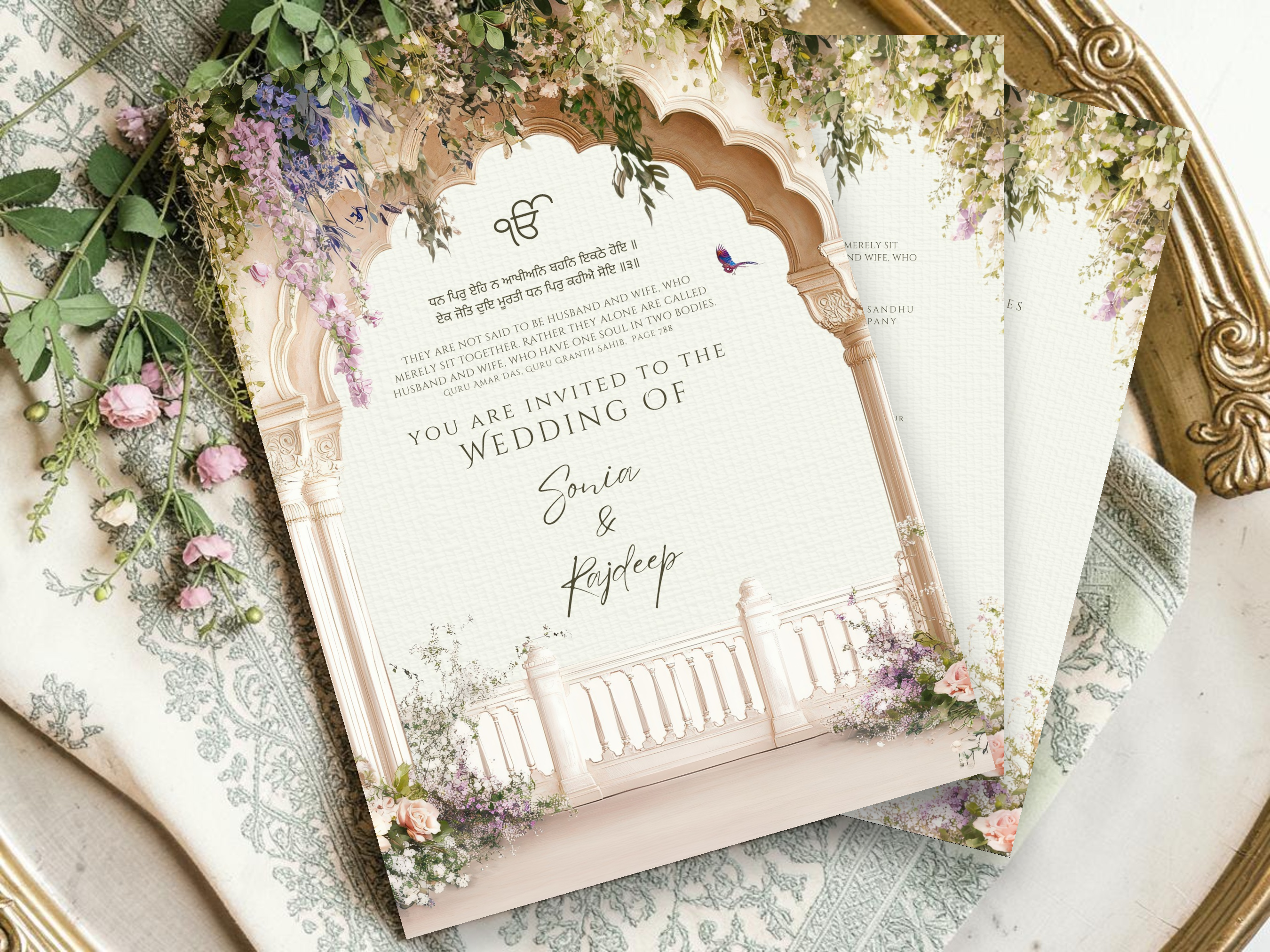 Close up of Sikh Anand Karaj digital wedding invitation cover page on a brass tray with wisteria botanical arch and Ik Onkar, showing Gurmukhi shabad and invitation wording for Sonia and Rajdeep by Krafty Kaur