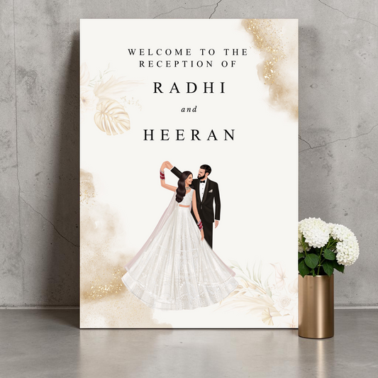 Personalised Indian wedding reception welcome sign leaning against a concrete wall, showing a bride in a white lehenga and groom in a black tuxedo dancing, with gold watercolour splashes and tropical leaf details